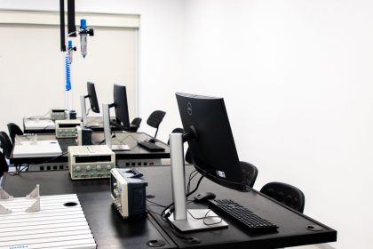 Laboratório de eletrônica com computadores, monitores e equipamentos técnicos dispostos em bancadas.