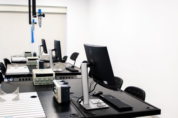Laboratório de eletrônica com computadores, monitores e equipamentos técnicos dispostos em bancadas.