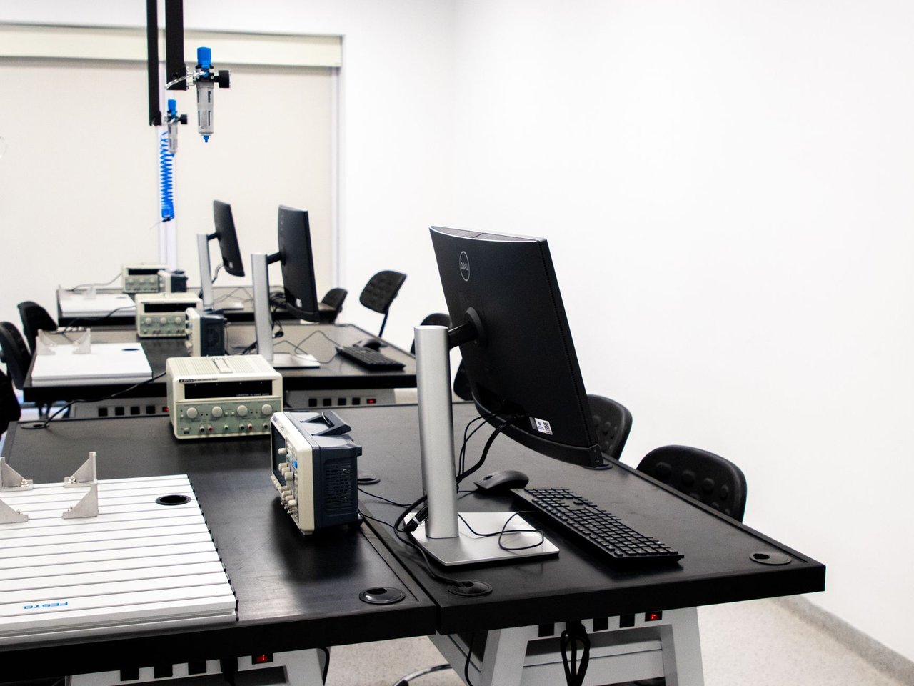 Laboratório de eletrônica com computadores, monitores e equipamentos técnicos dispostos em bancadas.