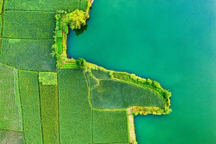 Vista aérea de áreas agrícolas coloridas ao lado de um corpo d’água em Rumpin, na Indonésia.