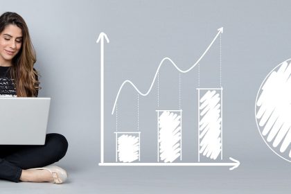 Mulher analisa gráficos e indicadores financeiros em um computador portátil.
